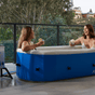 Two girls sitting in an inflatable hot tub having a drink with a scenic background
