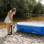 A girl outside on a rocky riverbed pump inflating a hot tub with Joolca branding