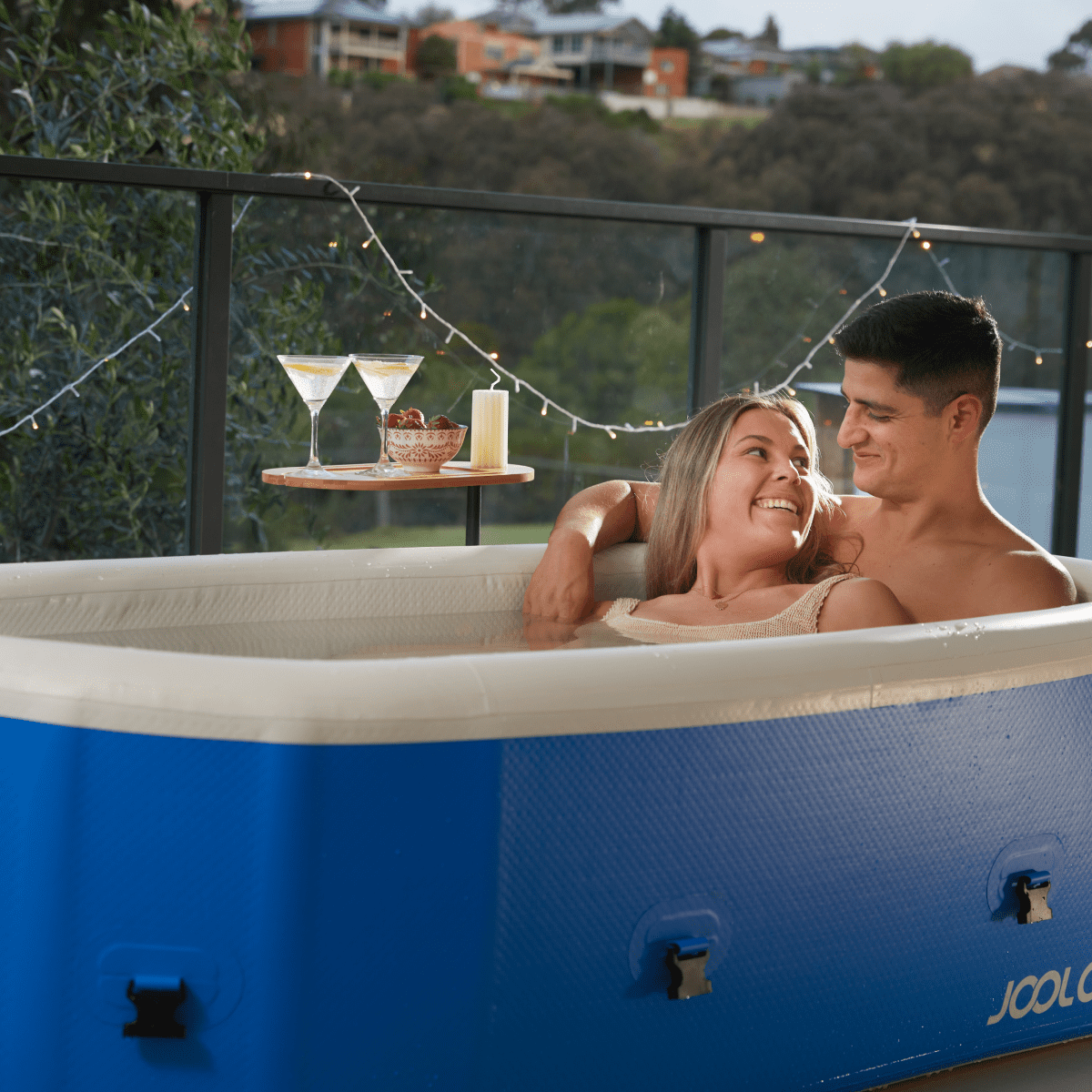 A man and woman sitting in an inflatable hot tub with a scenic background