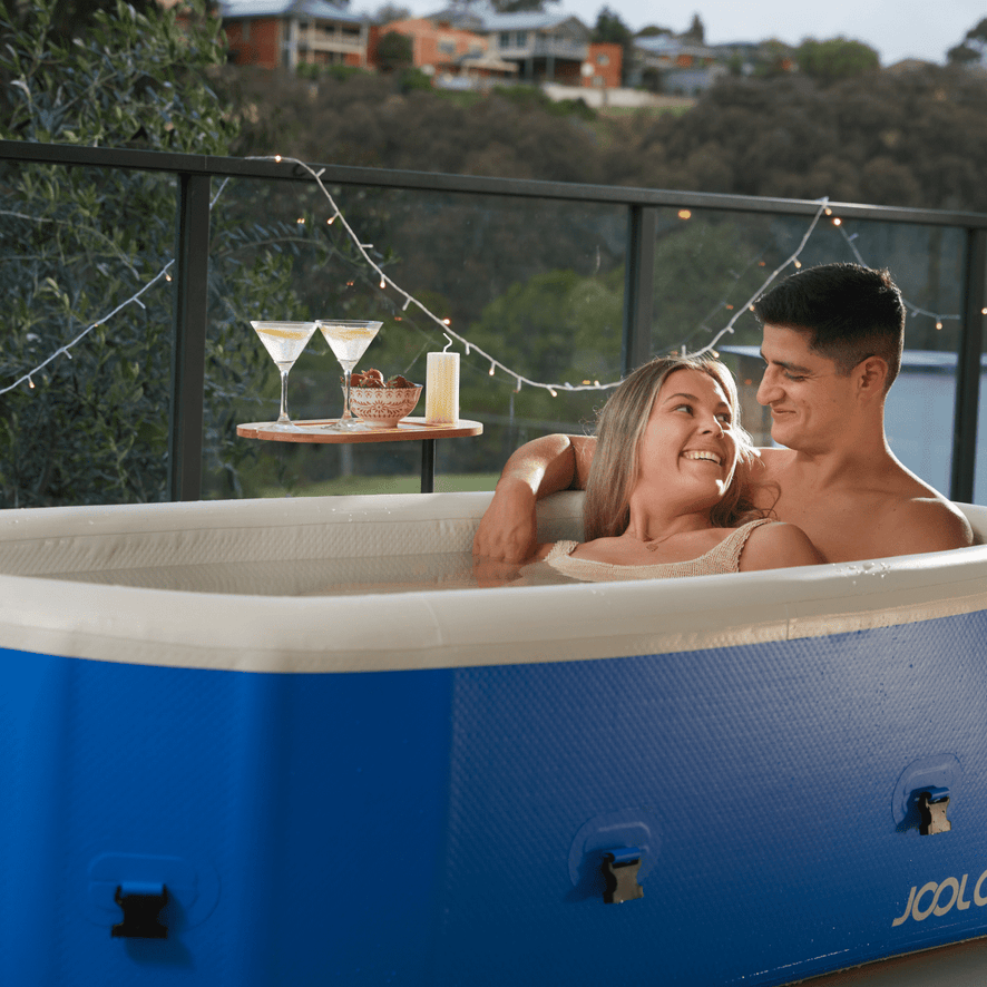 A man and woman sitting in an inflatable hot tub with a scenic background