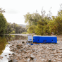 A lady taking a bath on a rocky river bed in an inflatable hot tub