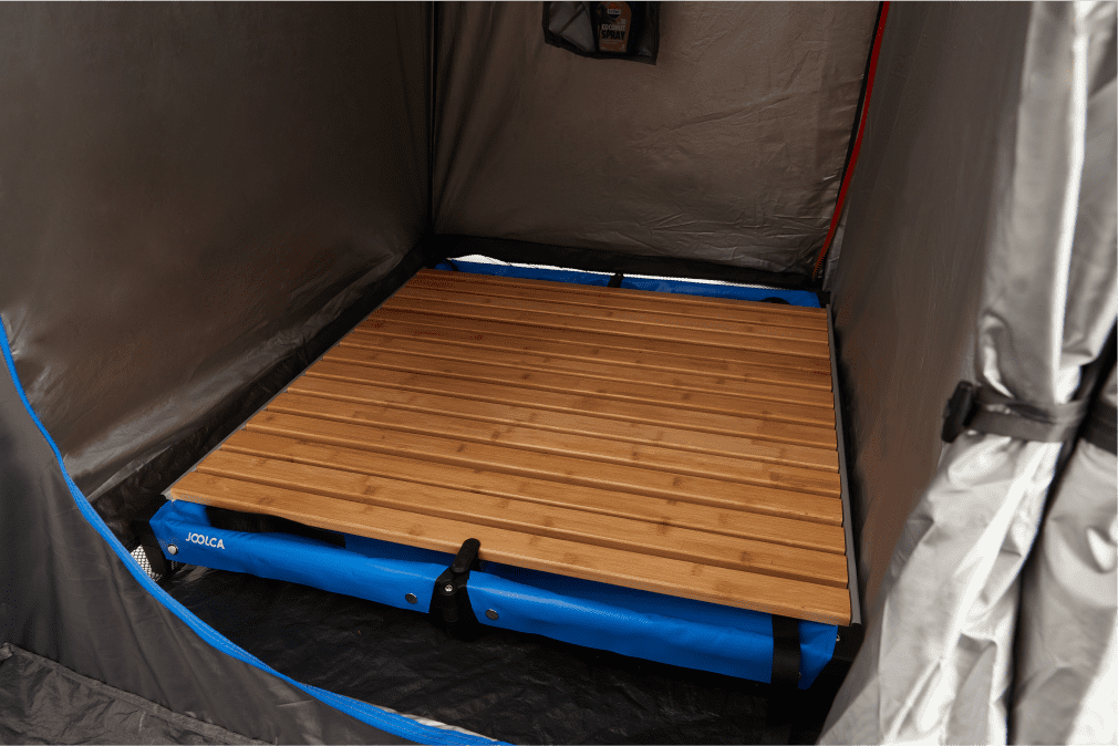 An internal look at a shower tent with a wooden shower base inside