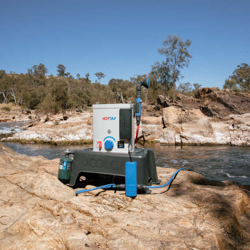 A portable hot water heater on a rocky river bed with a few accessories attached