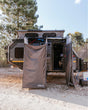 A Joolca branded mounted double tent attached to a caravan out on a dirt road surrounded by trees