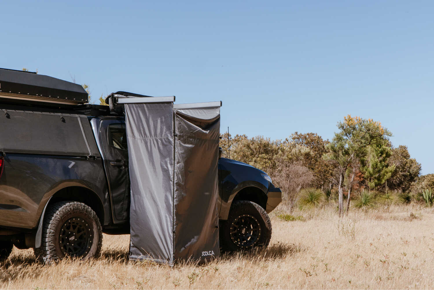 A mounted single tent attached to a 4WD, out in a dry grass patch