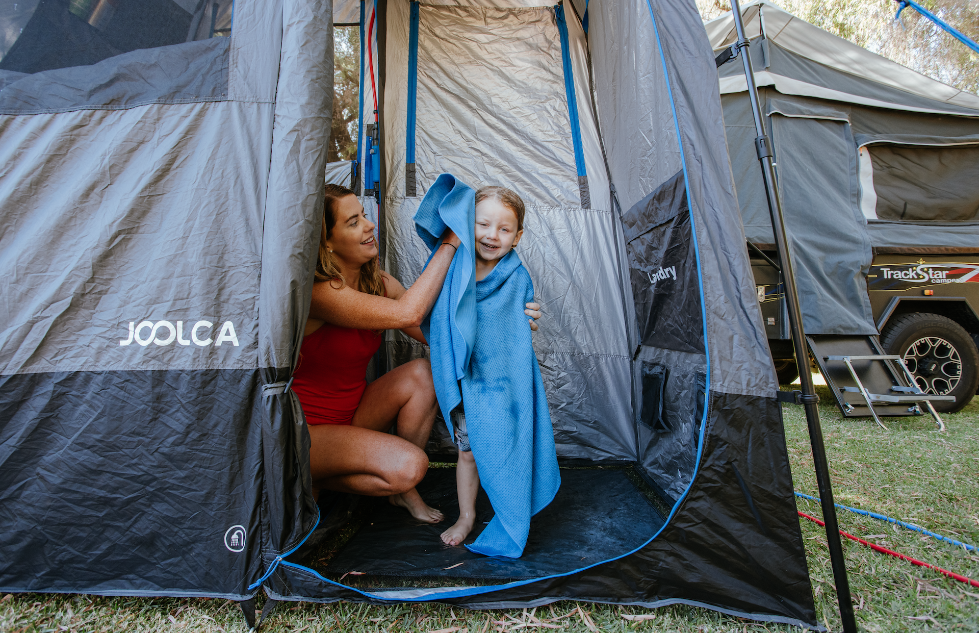 Woman and child standing in front of a Joolca tent, with the woman holding a blue towel.