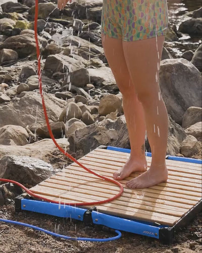Close-up of a hand and pant leg beside the bamboo slats of the Joolca Shower Base