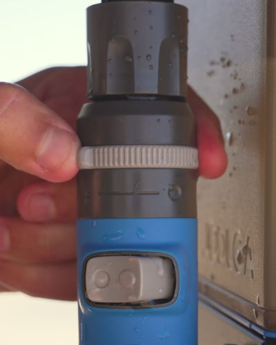 Close-up of hands holding the HOTTAP Go shower head running water by a river.