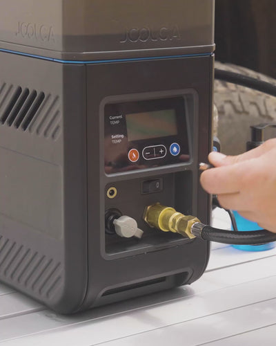 Person turning on the HOTTAP Go water heater with hoses connected outdoors.