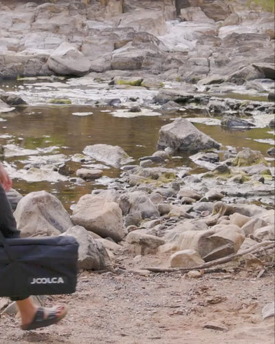 Woman showering outdoors on a rocky riverbank using the Joolca Shower Base