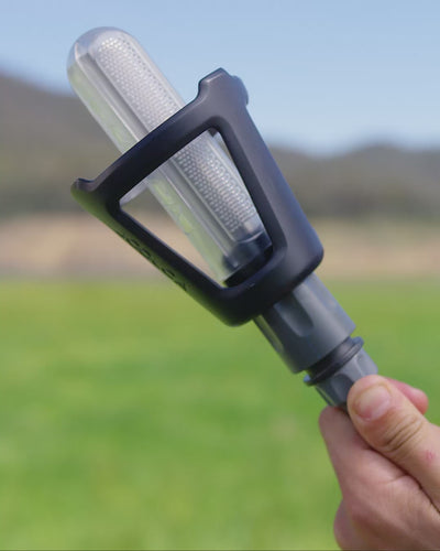 Hand holding the HOTTAP V2 River Pump with its two-stage filter, ready to drop into a creek or tank.