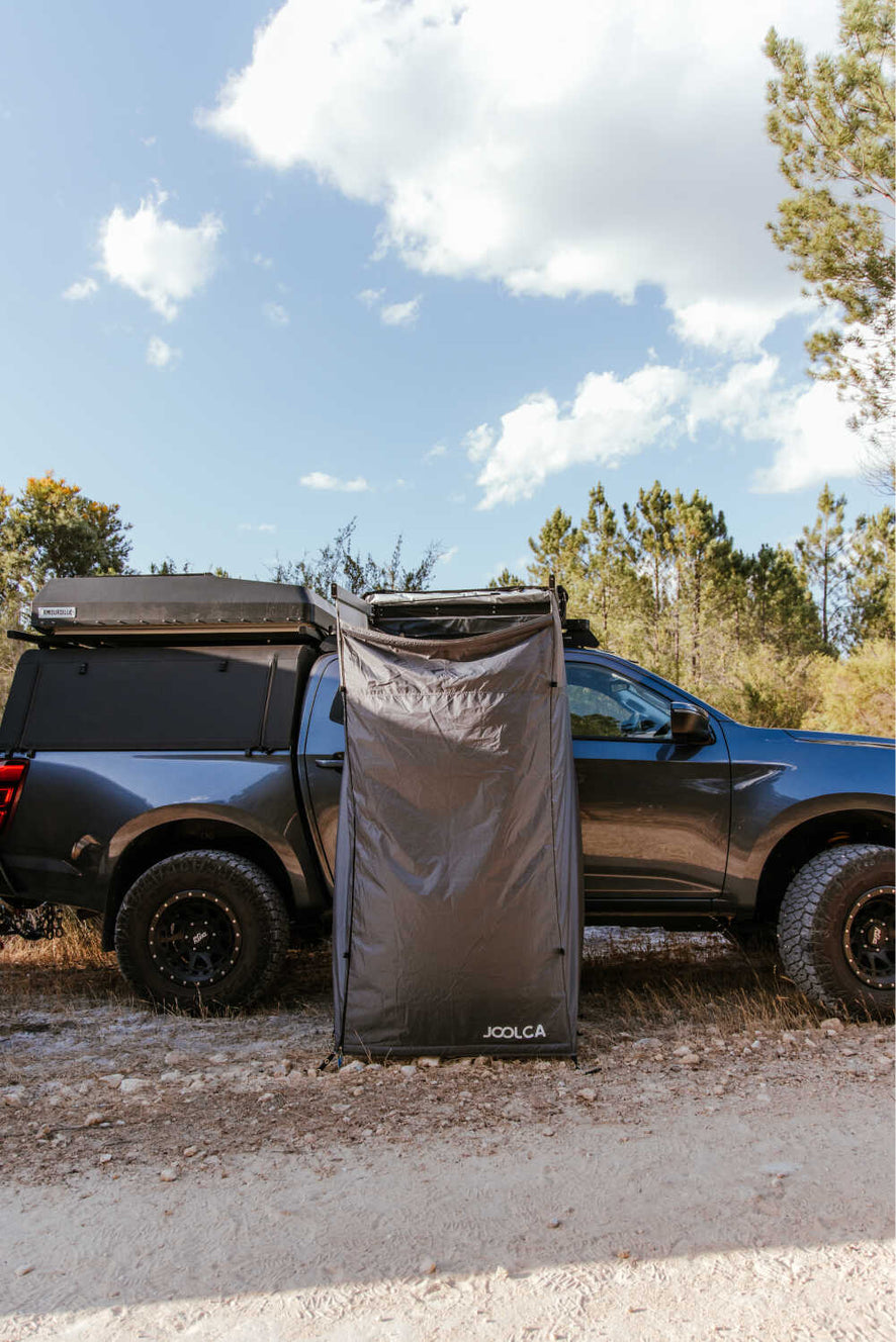 A Joolca branded mounted single tent attached to a 4WD out on a dirt road surrounded by trees